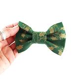 hand holding a green Christmas dog bow tie with gold holly leaves on a white background