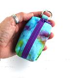 A ladies hand holding a blue tie dye fabric dog waste bag dispenser.